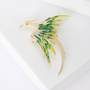 Close-up of luxury phoenix brooch with green zircon and gold wings on white display