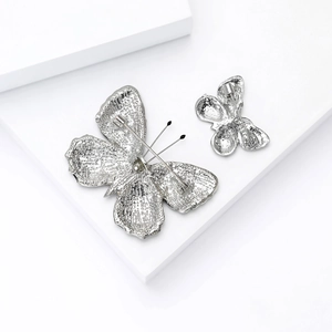 Detailed back view of silver butterfly brooches with secure pin mechanisms on white stands