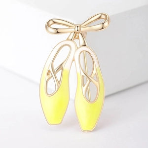 Détail de la broche ballerine en émail jaune dégradé avec nœud doré sur support blanc