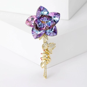 Détail de la broche rose avec cristaux bleus et main dorée ornée de zircons brillants