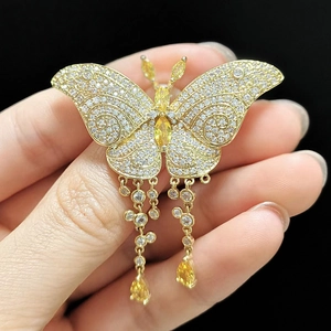 Gros plan d'une broche papillon en or avec ailes en zircon et pendentifs jaune vif