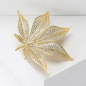 Detailansicht der goldfarbenen Ahornblatt-Brosche mit Zirkonia auf weißem Sockel