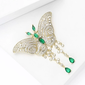 Détail macro d'une broche papillon avec pompons, zircons et gemmes émeraude vert