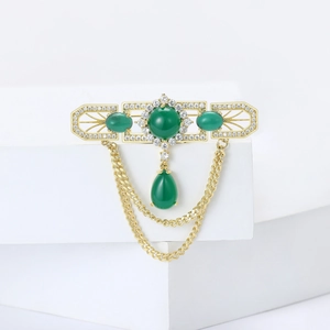 Luxury gold brooch with green gemstones and elegant tassel chains on white pedestal