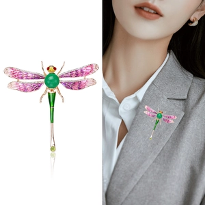 Creative dragonfly brooch with green gemstone and purple enamel wings on white background