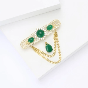 Close-up of vintage gold brooch with green gemstones, white zircon pavé, and tassel detail