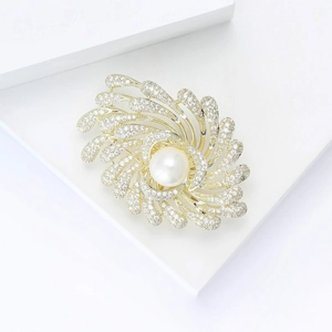 Détail macro d'une broche spirale dorée avec perle centrale et zircons micro-pave