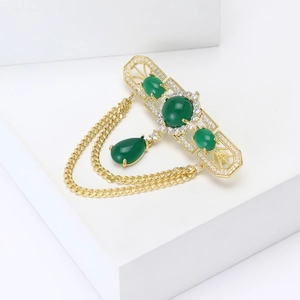 Close-up of vintage gold brooch with green stones, zircon micro-inlay and double chains
