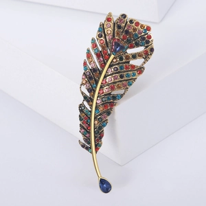 Macro detail of vintage gold feather brooch featuring colorful crystals and blue teardrop gem