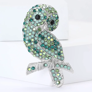 Spilla di lusso a forma di gufo con cristalli verdi e base in argento su sfondo bianco