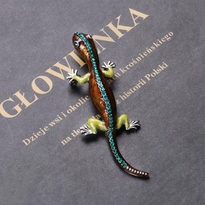 Detailed close-up of gecko brooch with brown enamel and green rhinestones on book