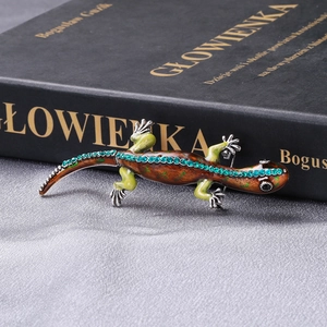 Macro detail of enamel gecko brooch with green rhinestones on silk fabric background