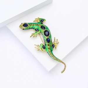 Détail macro d'une broche lézard verte de luxe avec cristaux bleus et alliage doré fini