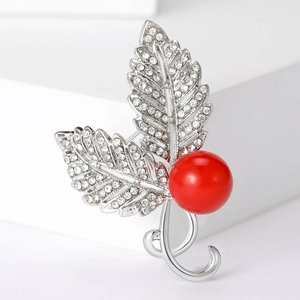 Macro detail of leaf-shaped brooch with silver zircons and a large red pearl ornament