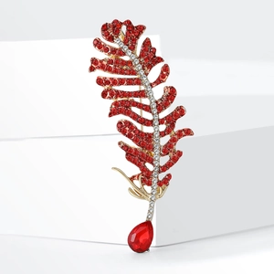 Elegant gold-tone feather brooch with red crystals and pear-cut gemstone on white stand