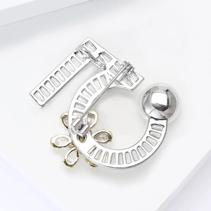 Détail macro d'une broche chiffre 5 argentée avec zircons et accents de pétales dorés