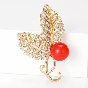Detail view of gold leaf brooch with white crystals and a vibrant red pearl accent