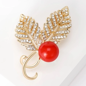 Detailed macro view of golden leaf brooch with white zircons and large red pearl bead