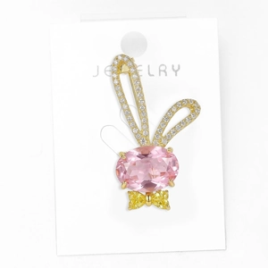 Détail macro d'une broche lapin en cristal rose avec oreilles dorées et nœud papillon jaune