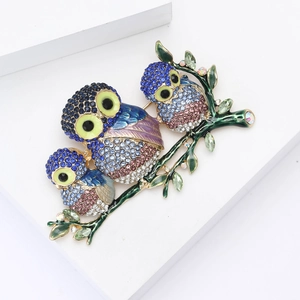 Détail d'une broche trois hiboux avec cristaux colorés et émail sur support blanc
