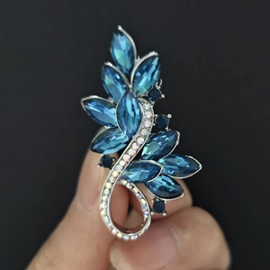 Detail of leaf-shaped brooch with deep blue crystals and rhinestones held in hand
