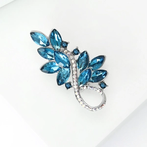 Detailed close-up of a vintage blue crystal brooch with silver metal floral leaf design