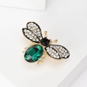 Close-up of golden bee brooch with emerald gemstone and sparkling crystal wings on white stand