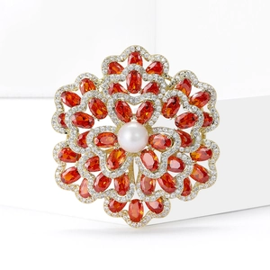 Eleganter Gold-Blumenbrosche mit orangen Zirkonia und Perle auf minimalistischem Stand