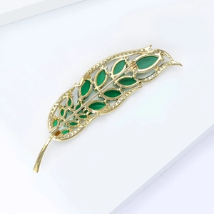 Detail view of golden feather brooch with green marquise stones and sparkling rhinestones