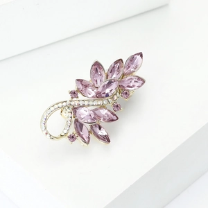 Close-up of pink crystal leaf brooch with gold metal details on a white surface