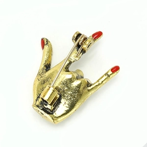 Detailed back view of a gold hand gesture brooch with metal pin buckle and red nail polish