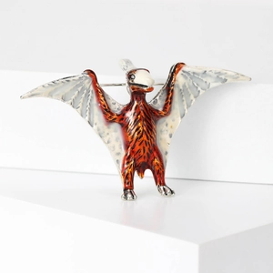 Detailed macro view of an orange pterodactyl brooch with silver metal edges and enamel finish