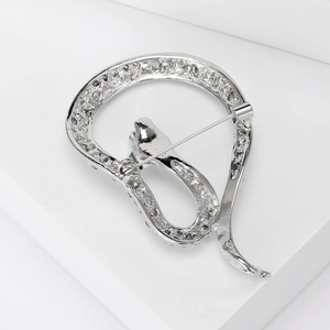 Detail view of silver snake brooch with green gem eyes and textured scales on white podium