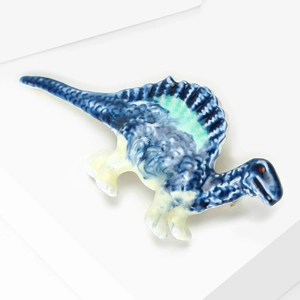 Detailed view of the blue Spinosaurus brooch featuring textured enamel and green accents
