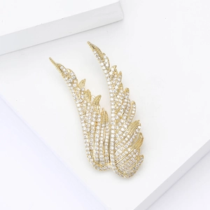 Spille ad ala dorate con zirconi brillanti su un supporto minimalista bianco elegante