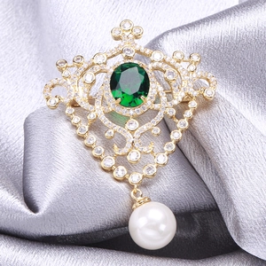Vintage gold medal brooch with emerald zircon and pearl drop on grey satin fabric