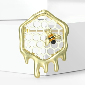 Gros plan d'une broche alvéolée dorée avec abeille en émail sur support blanc