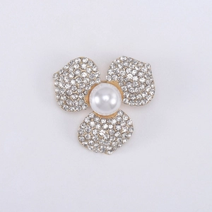 Gros plan d'une broche fleur dorée avec trois pétales en strass et une perle centrale