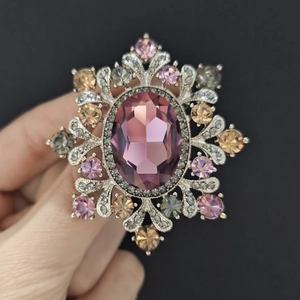 Macro shot of luxury vintage snowflake brooch with large purple oval crystal and multi-colored gems