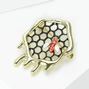 Détail d'une broche en forme de nid d'abeille dorée avec une abeille rouge et blanche