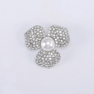 Détail de la broche fleur avec strass étincelants et une perle blanche centrale sur métal