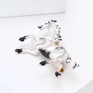 Detailed macro view of white enamel horse brooch with gold plating and black pattern accents