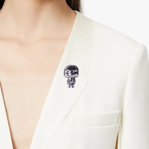 Polished alloy metal brooch with iconic designer figure worn on a white blazer