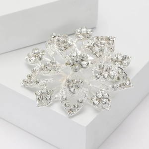 Elegant silver flower brooch with sparkling rhinestones displayed on white geometric blocks