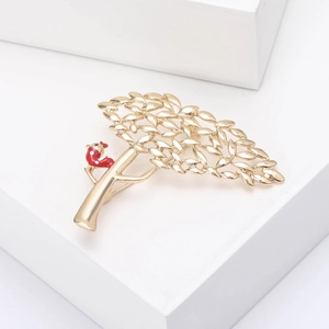 Vue détaillée d'une broche arbre dorée avec un oiseau rouge à pois sur un socle blanc