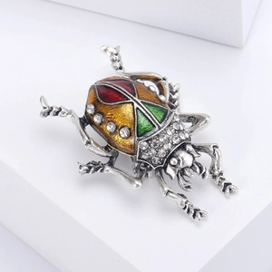 Detailed close-up of a vintage beetle brooch featuring colorful enamel and white rhinestones