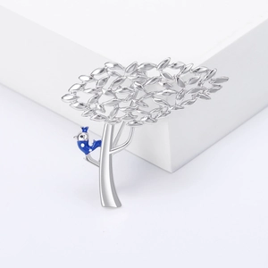 Broche arbre argentée avec oiseau en émail bleu sur fond de podium géométrique blanc