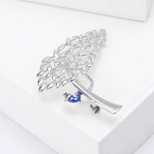 Détail de la broche arbre argentée avec oiseau bleu sur un support blanc moderne