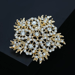 Macro view of gold flower brooch with white rhinestones on a black geometric stand