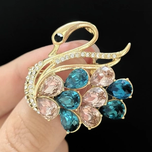 Detail of luxury gold plated swan brooch with multicolored crystals held by hand